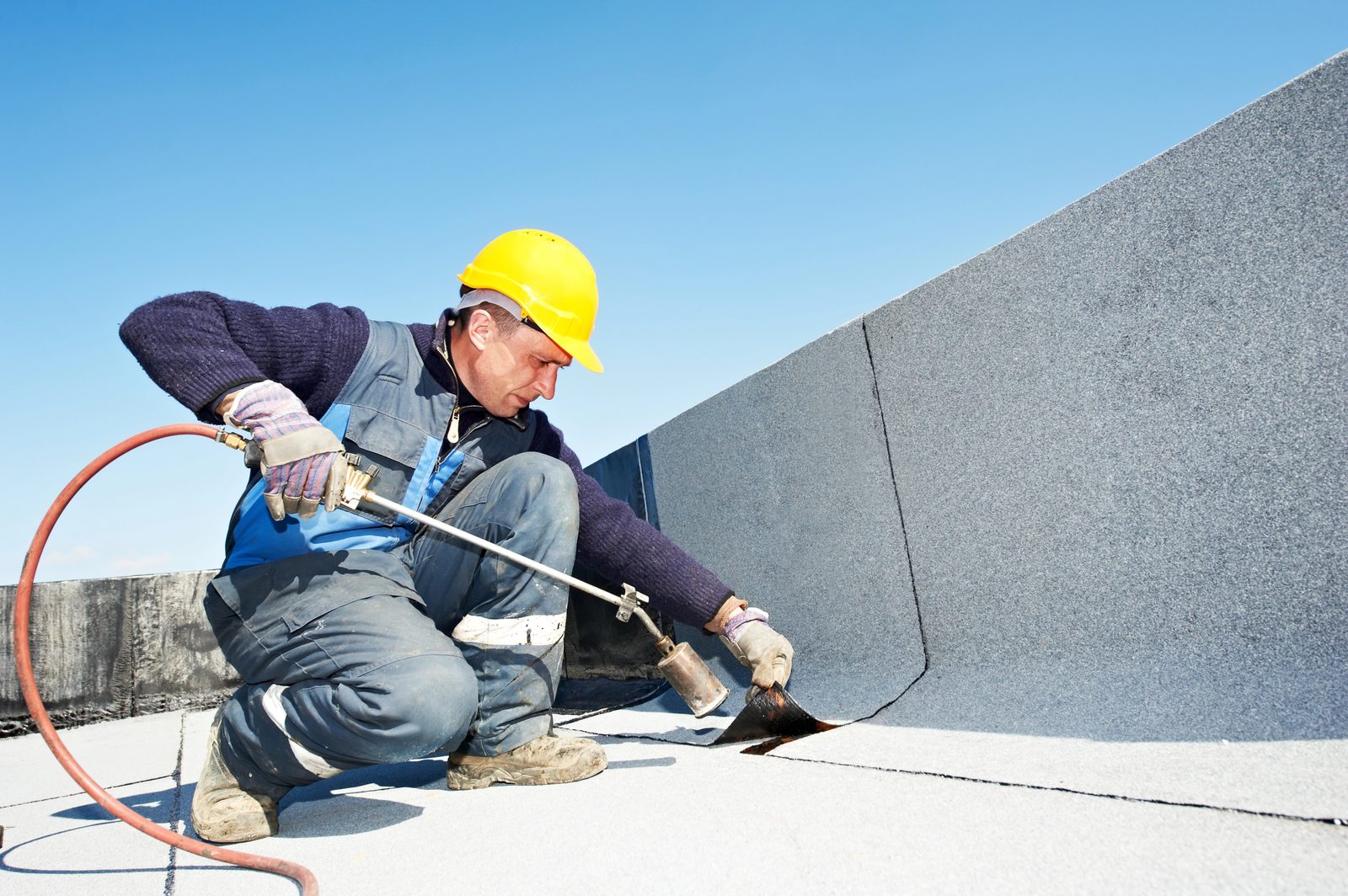 Roofer applying torch-down membrane on flat roof