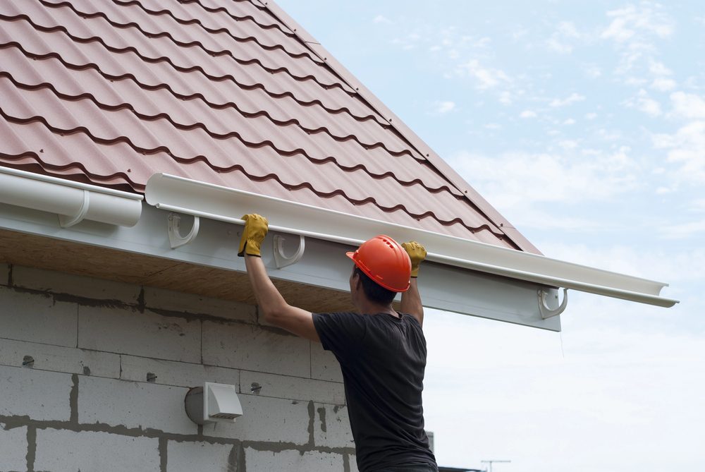 Worker installing white gutter on metal tile roof