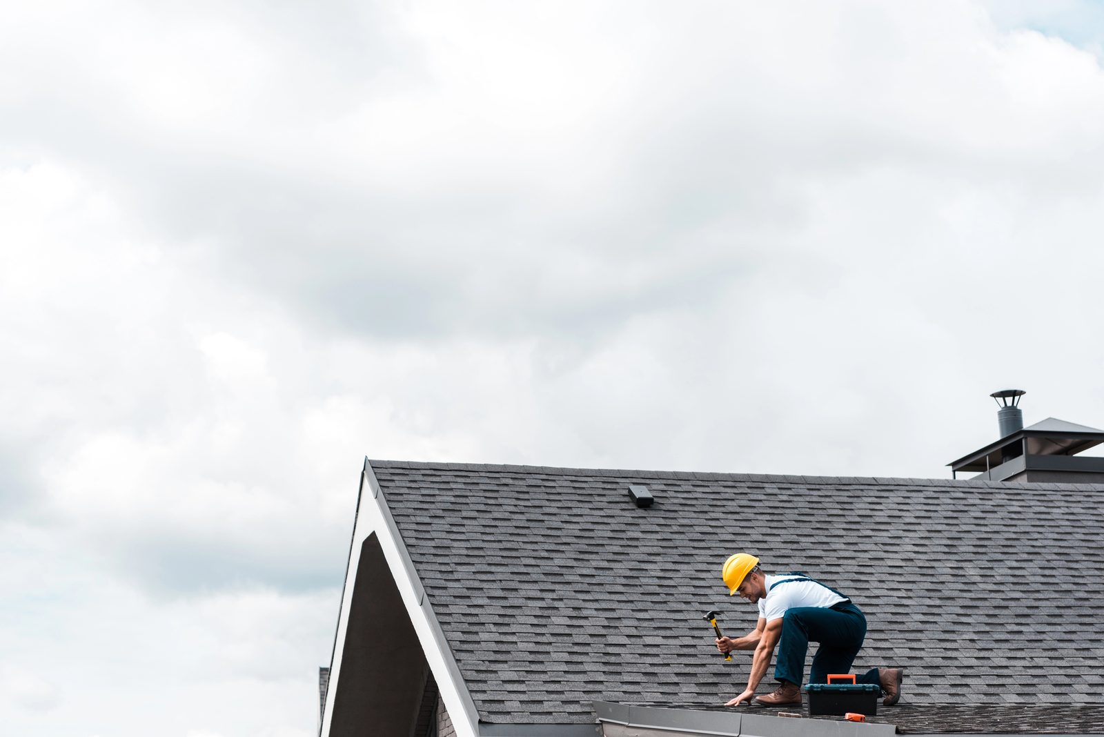 Roofer with hammer repairing shingle roof