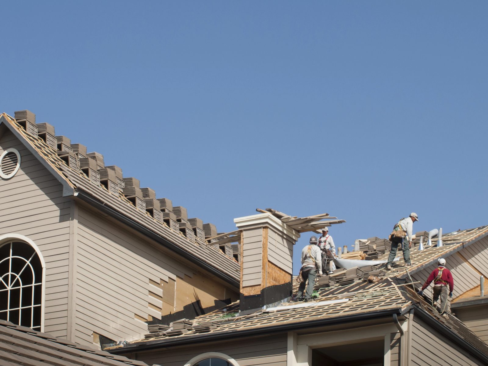 Roofing crew replacing tile roof on large home